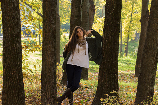 Beautiful white caucasian girl with blue eyes among trees in the forest on a sunny autumn day. The forest was full of brown fallen leaves on the ground.
