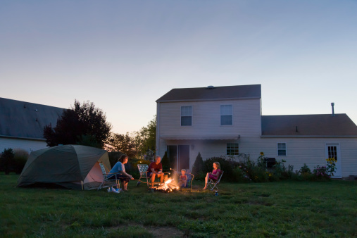 Family with two children, roasting marshmallows over a campfire in their backyard.