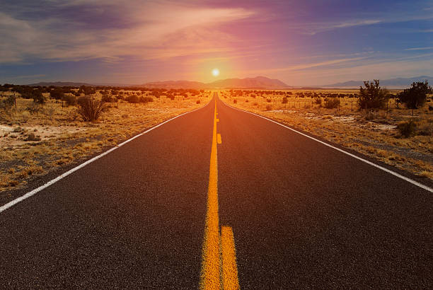 A dramatic sunset on an empty desert highway from the center of the road looking toward the horizon.