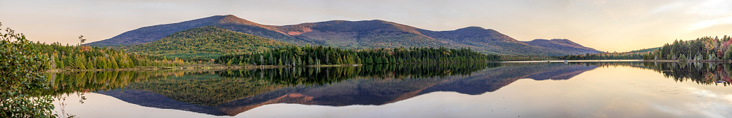 A panoramic view looking across a small lake to forested mountains. This is located in the Maine North Woods Highlands Region, Maine, USA. Multiple images used to create a panoramic.
