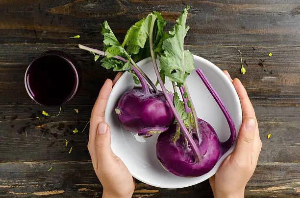 Purple kohlrabi in the bowl hold by hand on wooden background