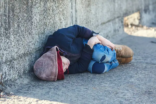 Photo of young homeless boy sleeping on the bridge