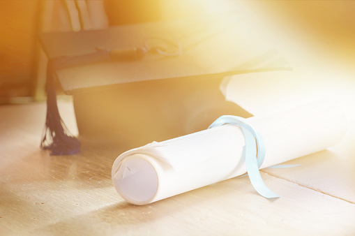 A mortarboard and graduation scroll, tied with blue ribbon, on a stack of old battered book with shallow depth of field