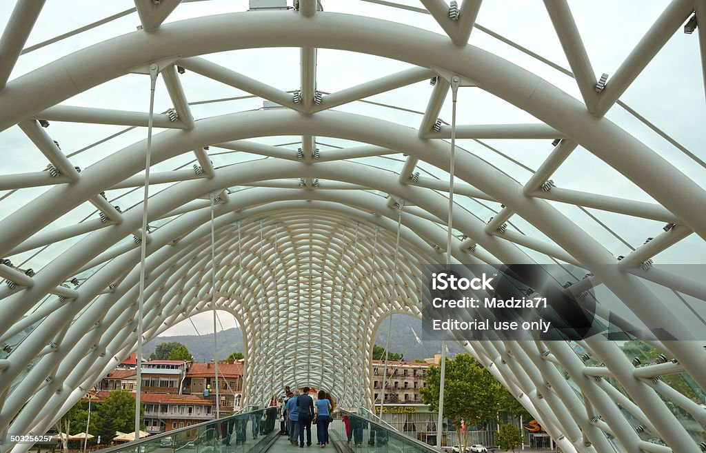 Tbilisi Thilisi, Georgia - July 1sr, 2014: Inside of the Bridge of Peace, close up. Some people walking on the brige. In the background - the old town district. Horizontal image in a cloudy day. Arch - Architectural Feature Stock Photo