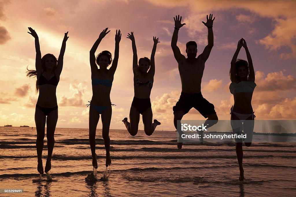 Multi ethnic friends having fun at the beach At sunset creating a very gorgeous sky and warm glow jumping for joy Adult Stock Photo