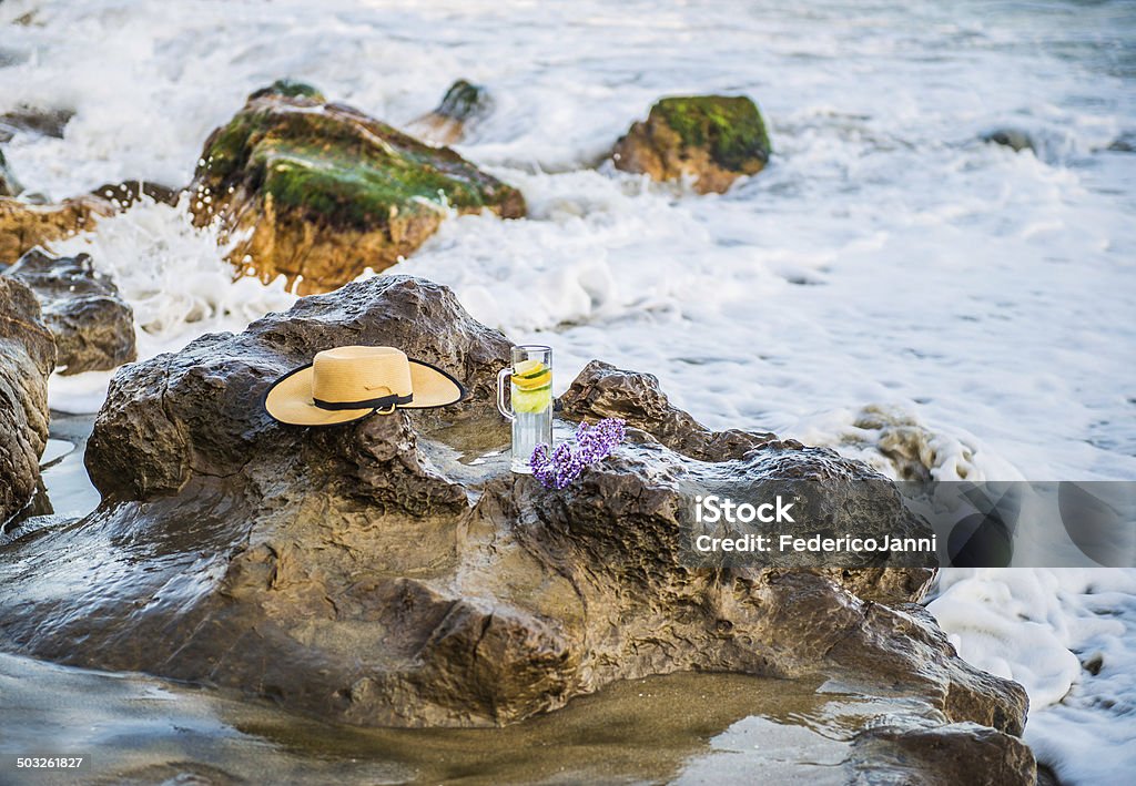 Glass and hat  on the water A glass of water and lemon and a woman hat on the rocks on the ocean Beach Stock Photo