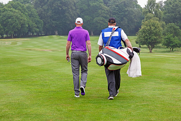 Golfer and caddy walking up a fairway stock photo