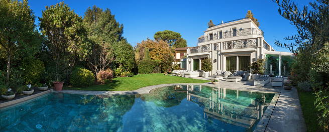 Architecture; beautiful house with pool, blue sky and lush garden