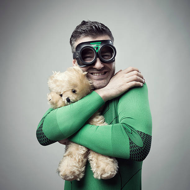 Smiling superhero cuddling a teddy bear Smiling cheerful superhero holding a cute teddy bear. man with teddy bear stock pictures, royalty-free photos & images