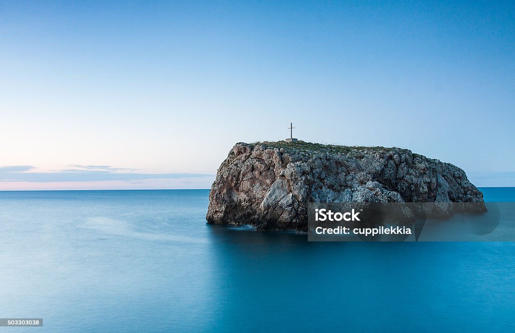 Hermit's Rock, polygnano a mare in Puglia View of the hermit's rock, along the coast of Polignano a Mare in Puglia; long exposure photograph at sunset with a view of the cross overlooking the rock. Blue Stock Photo