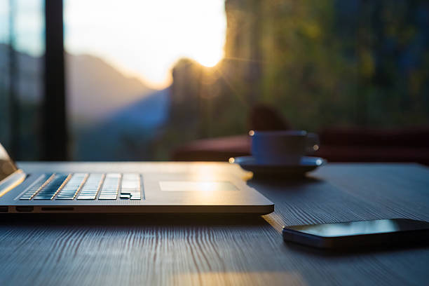 istock Computer Coffee Mug Telephone on black wood table sun rising 503306222
