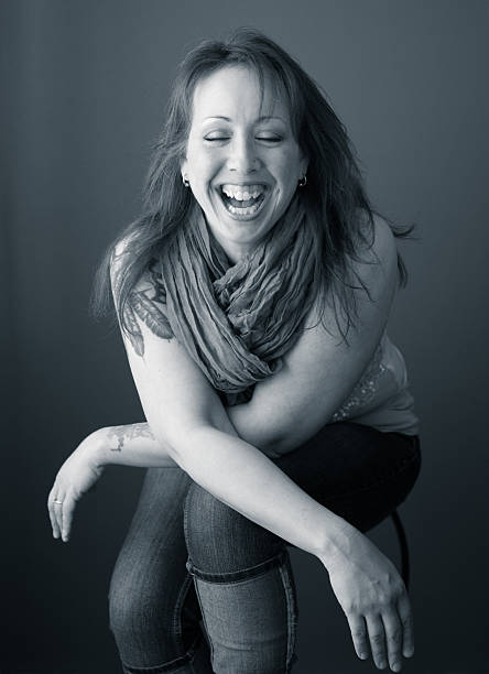 Casual young woman in red sweater sits on a floor, looks away and smiles. Side view. Full length studio shot isolated on white.