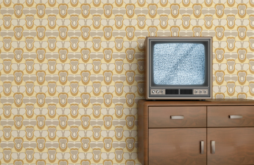 Vintage old television on wooden furniture and a interior background showing a sixties, seventies design wallpaper pattern. Television shows static signal, or \
