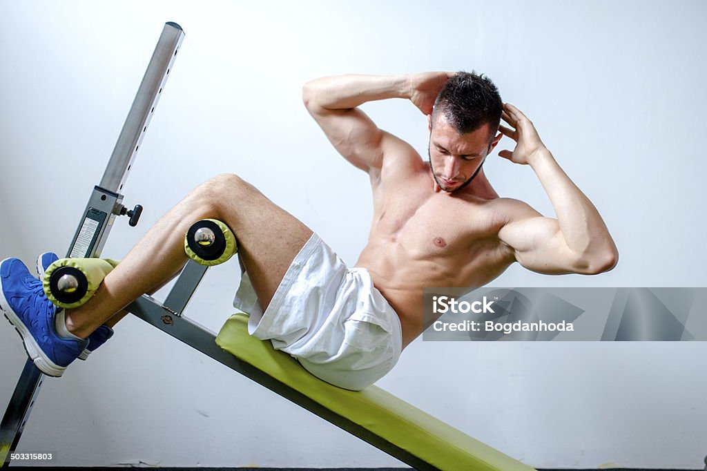 Handsome muscular man doing sit-ups on a incline bench Handsome muscular man doing sit-ups on a incline bench at fitness center or gym Abdomen Stock Photo