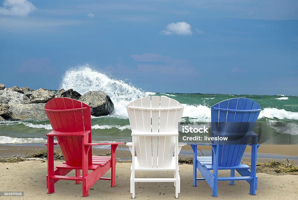 Adirondack chairs on beach Red, white and blue Adirondack chairs on beach with crashing waves on rocks. Beach Stock Photo