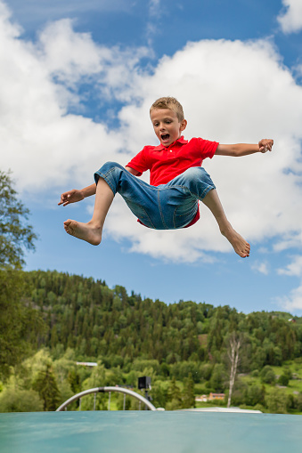 Young Scandinavian boy playing and having fun while jumping up and down on inflatable bouncing trampoline.