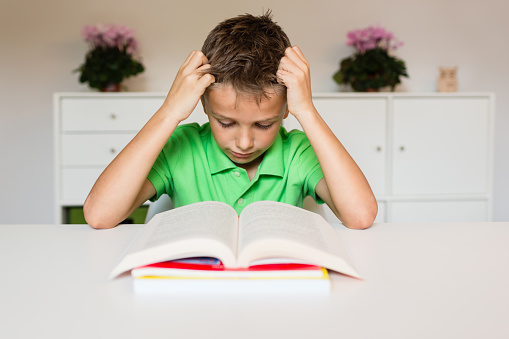 Young boy in green polo shirt having challenges reading a text in a school book.