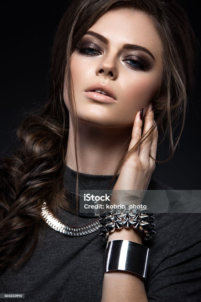 Beautiful girl with bright smokey make-up, perfect skin, black Beautiful girl with bright smokey make-up, perfect skin, black clothes, metal accessories and hairstyle as a braid. Picture taken in the studio on a gray background Fashion Model Stock Photo