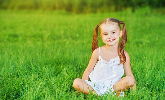 happy child little girl in a white dress lying on the grass Summer