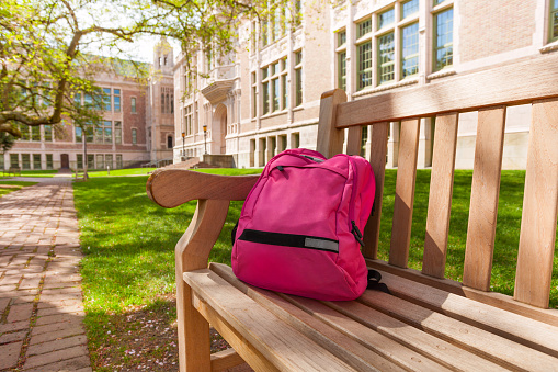 Backpack laying on the bench with educational buildings on the background after classes