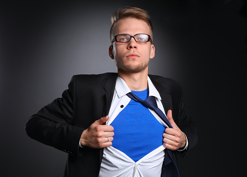 Young businessman acting like a super hero and tearing his shirt, isolated on gray background .