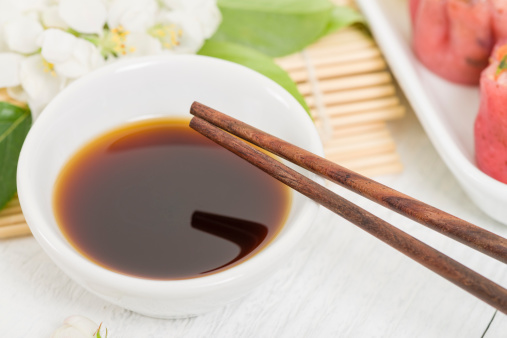 Close up of chopsticks resting on a small white bowl with asian dipping sauce.
