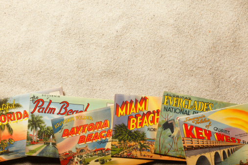 San Diego, California, USA - November 19, 2013: A group of vintage postcards showing various Florida tourist destinations on top of beach sand. Shot in a studio setting.