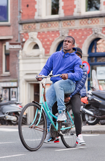 Amsterdam, The Netherlands - August 26, 2014: Young Surinam guy on a rusty blue bicycle with a classic building on the background According to the Amsterdam city council, 177 different nationalities residing in the Dutch capital, the world’s most multicultural city.