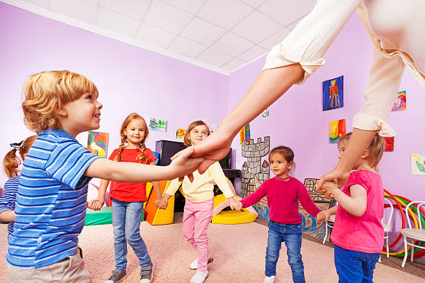 Group of boys and girls play roundelay with teacher in kindergarten class close view from bellow 