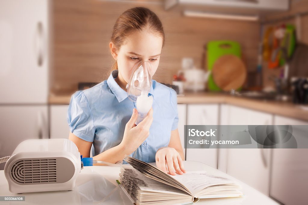 Chica haciendo inhalación y libro de lectura - Foto de stock de Inhalador de Asma libre de derechos