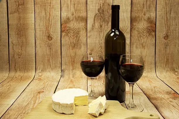 Two wine glasses with red wine,bottle of red wine and Camembert cheese against the curved wooden planks.Wooden background.