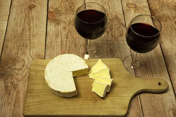Two wine glasses with red wine,bottle of red wine and Camembert cheese against the curved wooden planks.Wooden background.Horizontal view from the top.