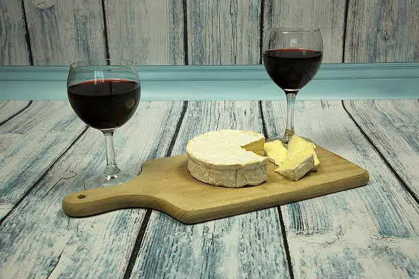 Two wine glasses with red wine and Camembert cheese against the vintage,blue wooden backgrounds.