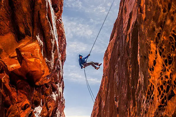 A rock climber kicks off the wall while descending into a slot canyon in Red Rock National Recreation Area
