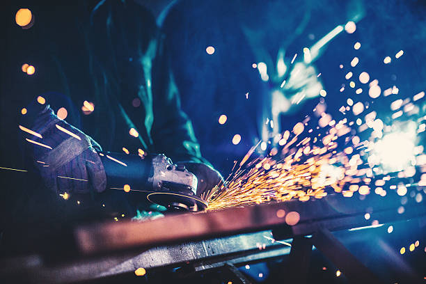 Metal industry routine. Closeup of heavy industry workers. One of the workers is welding two pieces of metal with arc welding machine. The guy in focus is grinding what his colleague just welded. He's using electric grind stone machine. Deep blue toned shot. grind stock pictures, royalty-free photos & images