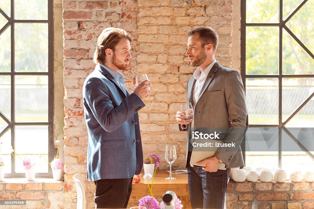 Two businessmen after work Two businessmen wearing smart casual jacket meeting after work, standing against brick wall, drinking water and talking.  Men Stock Photo