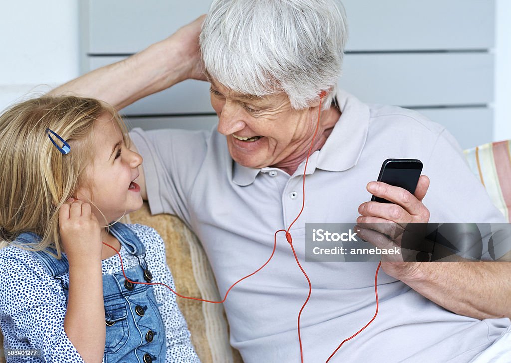 Sharing their love of music Shot of an adorable little girl listening to music from a cellphone with her grandfather Active Seniors Stock Photo