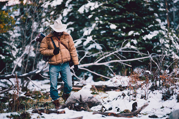 Man carries camping gear while walking through snowy woods