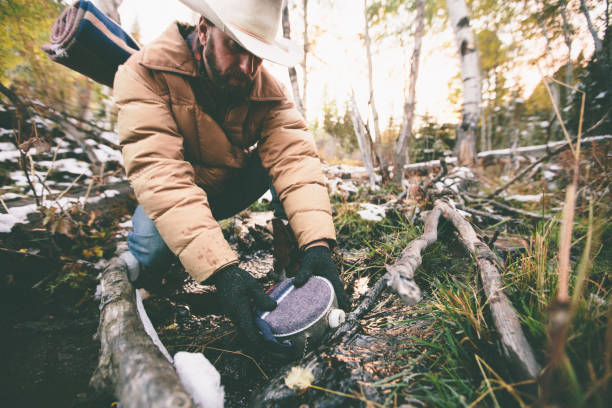Man fills water canteen while hiking through woods during winter