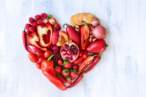 Collection of fresh red vegetables and fruits arranged in a heart shape on white rustic background strawberry raspberry pomegranate peppers capsicum chili potato beans legumes