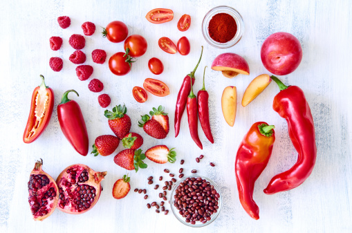 Collection of fresh red toned vegetables and fruits raw produce on white rustic background, peppers capsicum chili strawberry raspberry pomegranate tomato paprika azuki beans plum