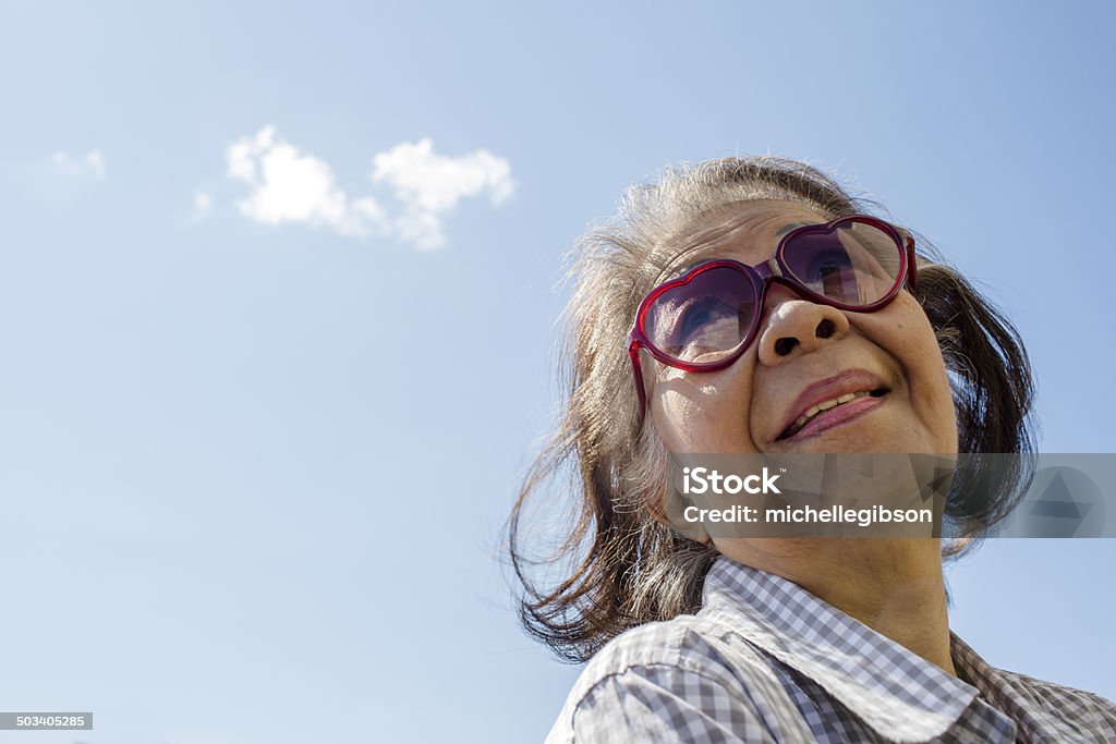 Anziani donna con occhiali da sole contro il cielo cuore - Foto stock royalty-free di Simbolo di cuore