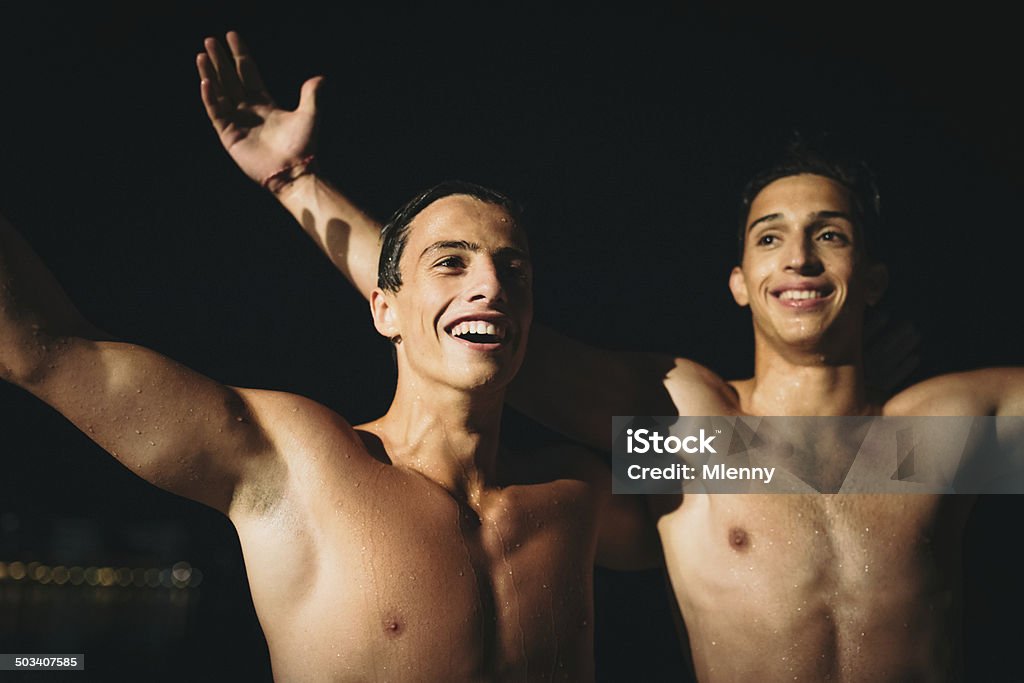 Athletes and the Victory Young athletes celebrating together the victory right after finishing the last swimming competition at night. Natural Light, High ISO. Swimming Stock Photo