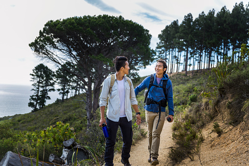A photo of young hikers walking on hill and talking. Full length of travellers in nature. Males are in casuals during vacation.