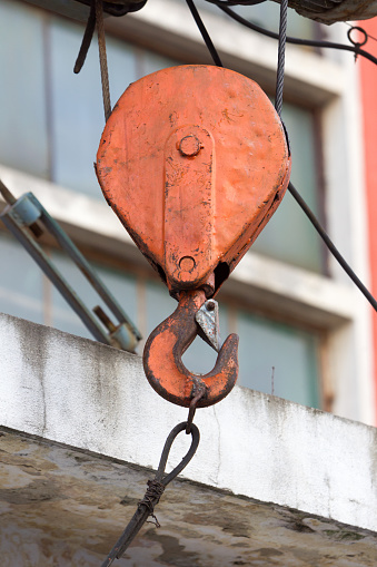 Rusty old red crane hook seen outside.