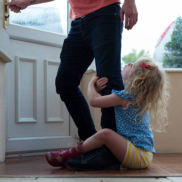 Don't go dad! A little girl clings to her fathers leg as he tries to leave their family home, she looks upset and pleading with him not to leave. gripping stock pictures, royalty-free photos & images