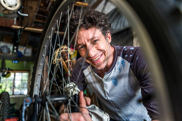 Portrait of worker cleaning cycle A photo of mature mechanic cleaning bicycle. Portrait of worker is repairing cycle. He is using cloth to wipe vehicle parts in workshop. Focus is on his face. bike workshop stock pictures, royalty-free photos & images