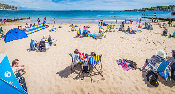 海辺での日光浴、ご家族連れのお客様や観光客の夏のビーチの休日のパノラマ - swanage ストックフォトと画像