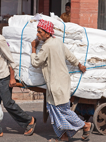 Delhi, India - March 22, 2014: Heavy load being moved by porters  through traffic in the heart of the old city. The use of porters to transport goods consignments in this way is common in Indian towns and cities