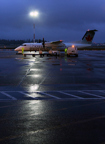 Victoria,Canada-December 27,2015:   Air Canada Express Propeller plane landed on the Victoria Airport Tarmac at Night. Wet and rainy. Luggage cart ready. 